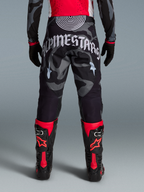 Spodnie Techstar Beast Coast w szarym kamuflażu, duże białe logo z tyłu, czarno-czerwone buty motocrossowe.