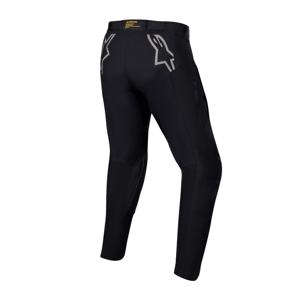 Spodnie Alpinestars Techdura, czarne spodnie enduro i off-road, widok z tyłu z szarymi logo gwiazdy na biodrach, żółte oznaczenia marki na tylnym pasie, wytrzymały, rozciągliwy materiał poliamidowy o trwałej konstrukcji do jazdy motocyklem