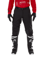 Alpinestars Techdura Pants, spodnie enduro i off-road, czarne, noszone z czerwoną bluzą Alpinestars i czarno-białymi butami, wytrzymała konstrukcja z rozciągliwego płótna, regulowana magnetyczna klamra paska, skórzane wzmocnienia na kolanach dla lepszej wydajności off-road