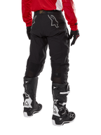 Alpinestars Techdura Pants, spodnie enduro off-road, czarne, widok z tyłu pokazujący szare logo gwiazdy na siedzeniu, noszone z czerwoną koszulką z długim rękawem i czarno-białymi butami Tech 7, wytrzymała konstrukcja tekstylna do jazdy typu adventure