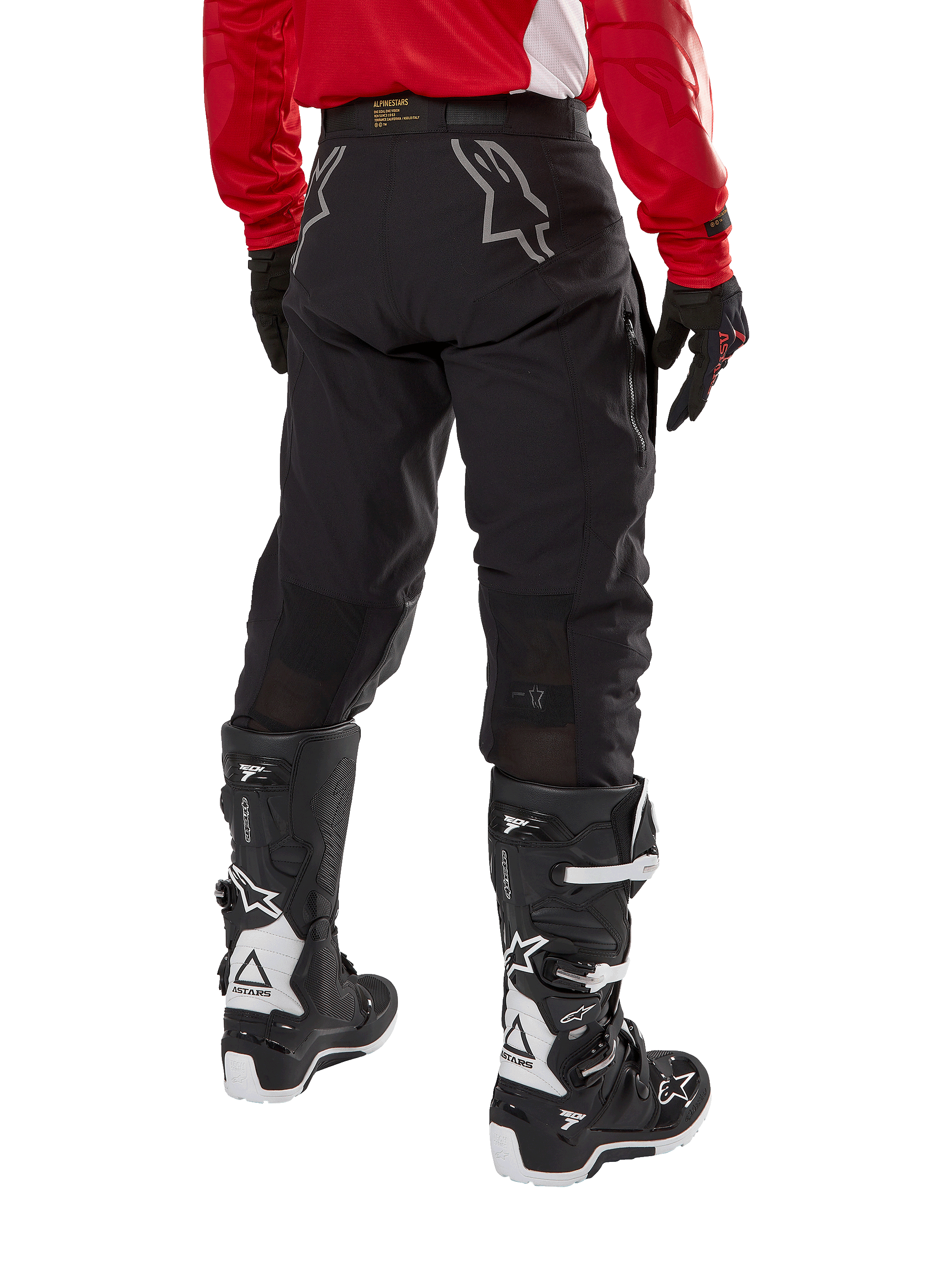 Alpinestars Techdura Pants, spodnie enduro off-road, czarne, widok z tyłu pokazujący szare logo gwiazdy na siedzeniu, noszone z czerwoną koszulką z długim rękawem i czarno-białymi butami Tech 7, wytrzymała konstrukcja tekstylna do jazdy typu adventure
