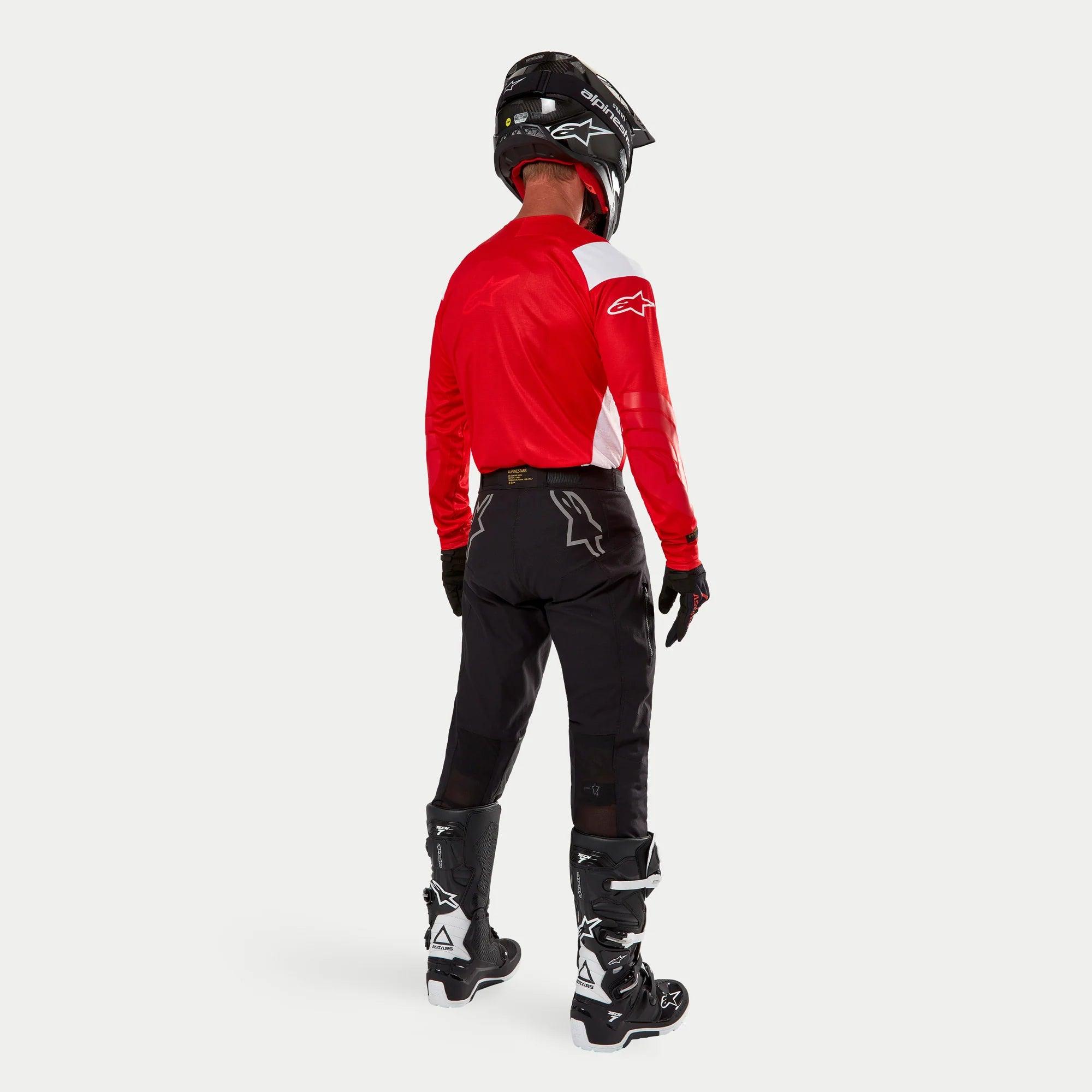 Spodnie Alpinestars Techdura, spodnie enduro off-road, czarne, widok z tyłu na motocykliście w czerwono-białej bluzie i czarno-białych butach, z białym logo gwiazdy z tyłu oraz wytrzymałą, techniczną, rozciągliwą konstrukcją.