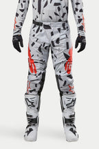 Spodnie Alpinestars Techstar Rantera 2024, spodnie motocrossowe, Haze Gray Camo, noszone z pasującą koszulką, czarnymi rękawicami i białymi butami, z czarnym wzorem w plamy i czerwonym brandingiem Alpinestars, wytrzymała konstrukcja do wyścigów off-road