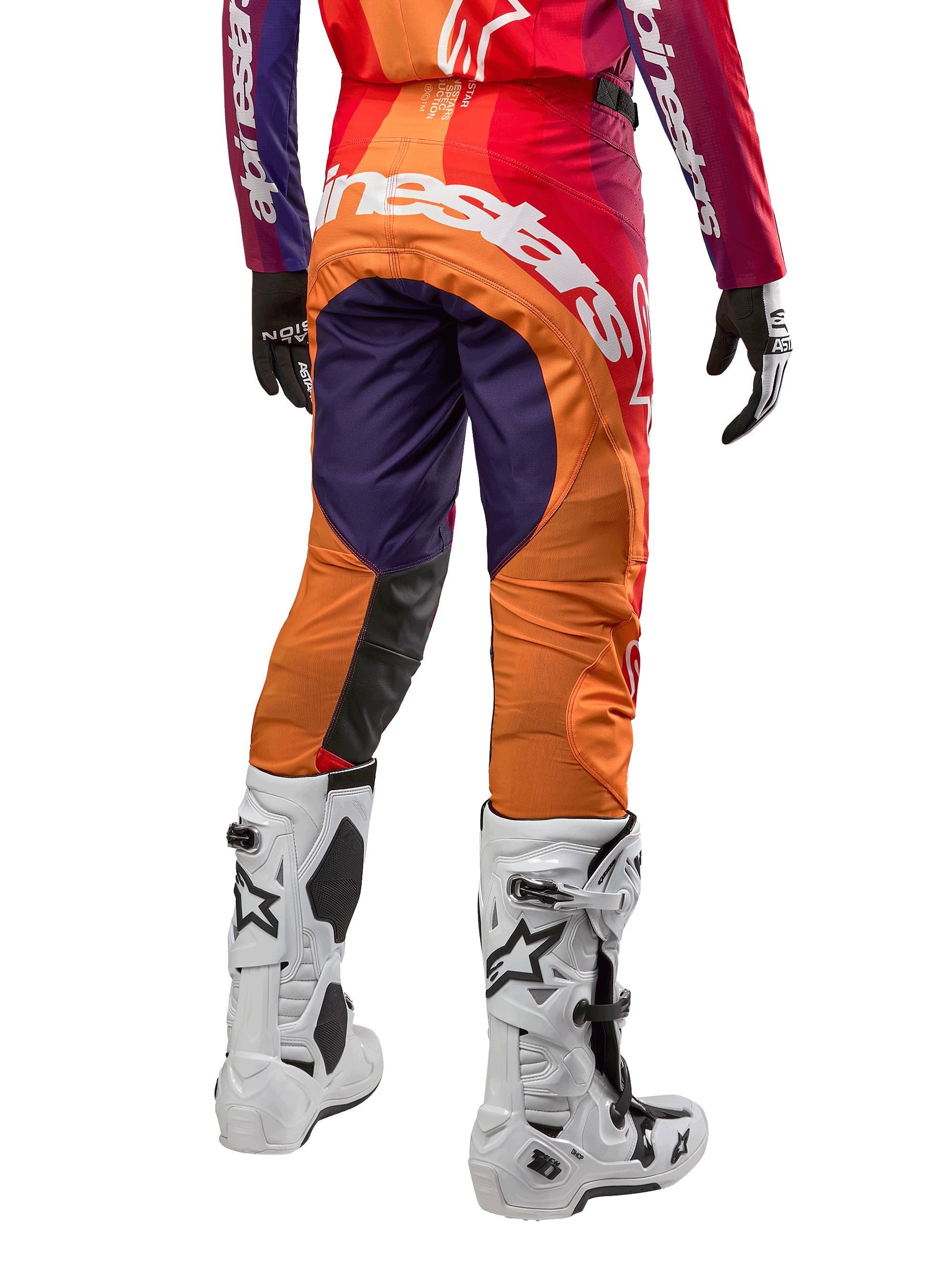Alpinestars Techstar Pneuma Pants 2024, spodnie motocrossowe, fioletowe, pomarańczowe i granatowe z czerwonymi akcentami, duże białe logo na siedzeniu, widok od tyłu z białymi butami i czarnymi rękawicami, sportowy design