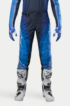 Spodnie Alpinestars Techstar Pneuma 2024, spodnie motocrossowe, granatowe i jasnoniebieskie, noszone z pasującą niebieską bluzą i białymi butami, z białym brandingiem Alpinestars i zapięciem na magnetyczną klamrę, zaprojektowane dla profesjonalnej wydajności off-road