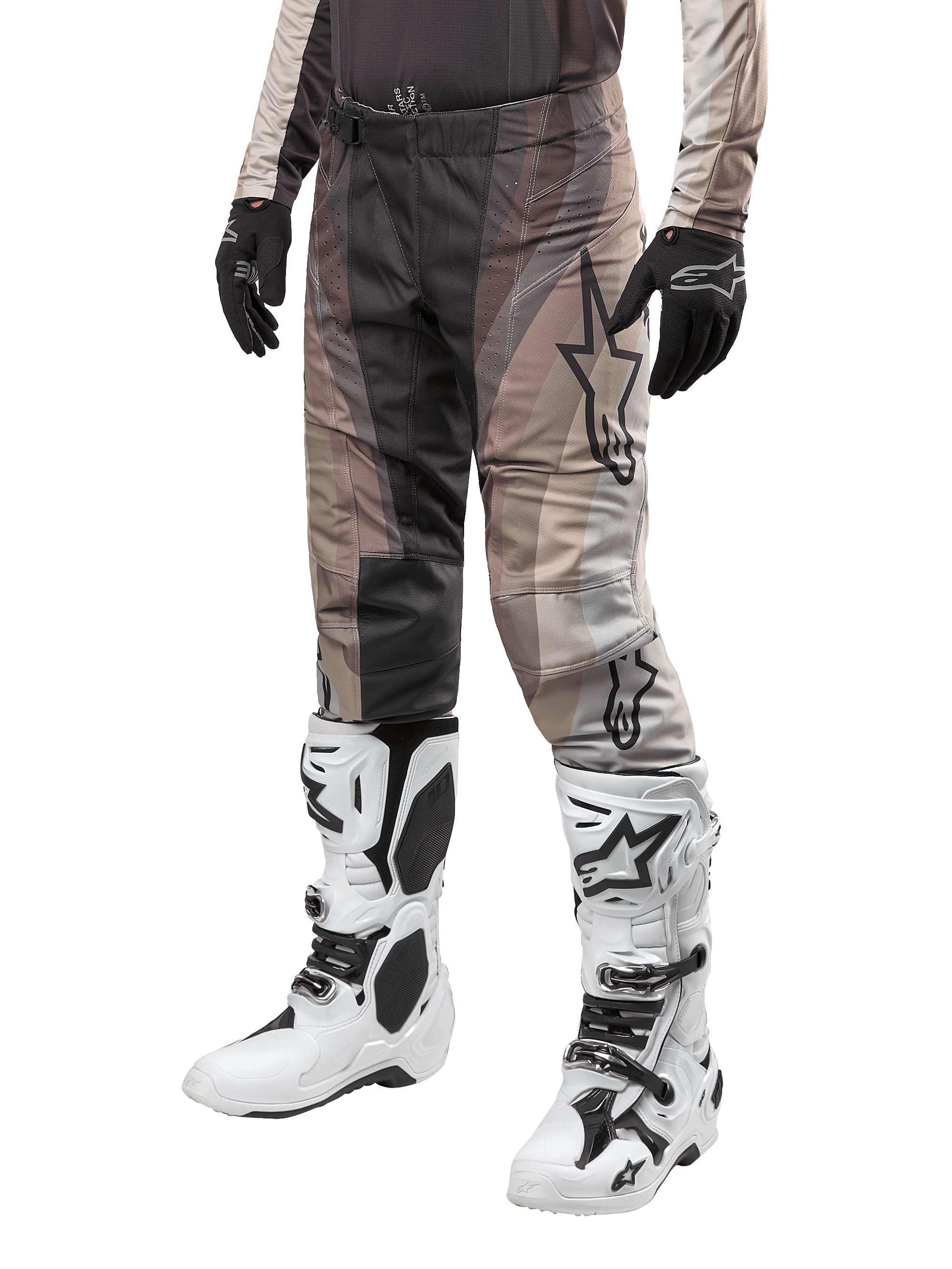 Spodnie Alpinestars Techstar Pneuma 2024, spodnie motocrossowe, w kolorach ciemnego piasku i szarym, noszone z biało-czarnymi butami i czarnymi rękawicami, z falistym wzorem i dużym logo gwiazdy, wytrzymała odzież do wyścigów terenowych