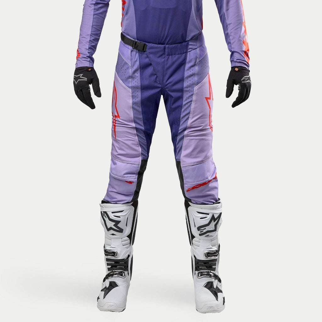 Alpinestars Techstar Ocuri Pants 2024, spodnie motocrossowe, fioletowe z jaskrawopomarańczowymi akcentami, sportowy krój wyścigowy, białe buty i czarne rękawice, laserowe perforacje dla lepszej wentylacji