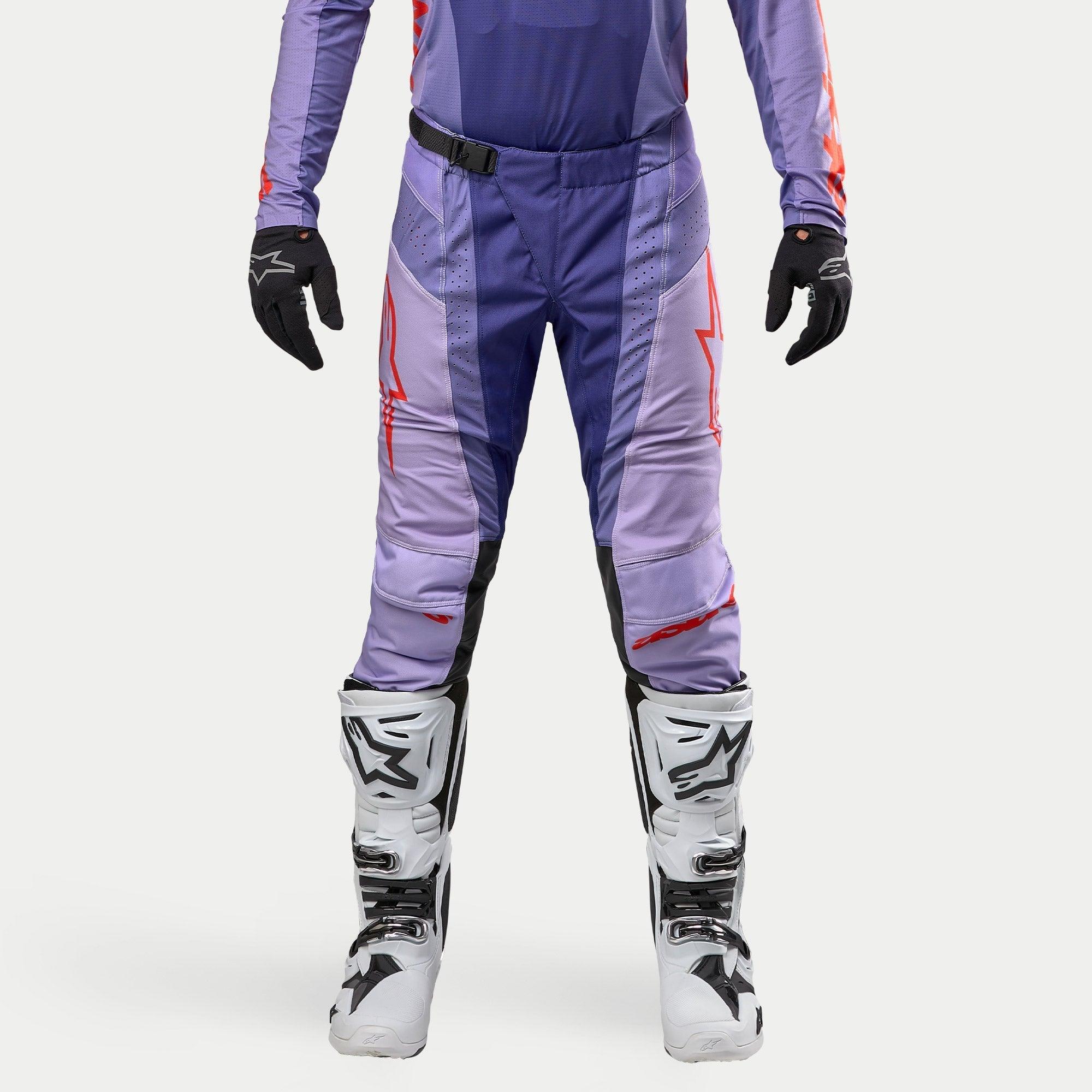 Alpinestars Techstar Ocuri Pants 2024, spodnie motocrossowe, fioletowe z jaskrawopomarańczowymi akcentami, sportowy krój wyścigowy, białe buty i czarne rękawice, laserowe perforacje dla lepszej wentylacji