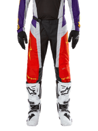 Spodnie Alpinestars Techstar Ocuri 2024, spodnie motocrossowe, jaskrawopomarańczowe, fioletowe i czarne, noszone z pasującą koszulką, czarnymi rękawicami i białymi butami, posiadają jaskrawopomarańczowe panele przednie, fioletowe akcenty w pasie i perforowane szare sekcje, techniczny design do wyścigów off-road