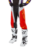 Spodnie Alpinestars Techstar Ocuri 2024, spodnie motocrossowe, jaskrawopomarańczowe, czarne i białe z żółtą grafiką gwiazdy, noszone z fioletową bluzą i białymi butami, wytrzymała odzież wyczynowa do zawodów terenowych