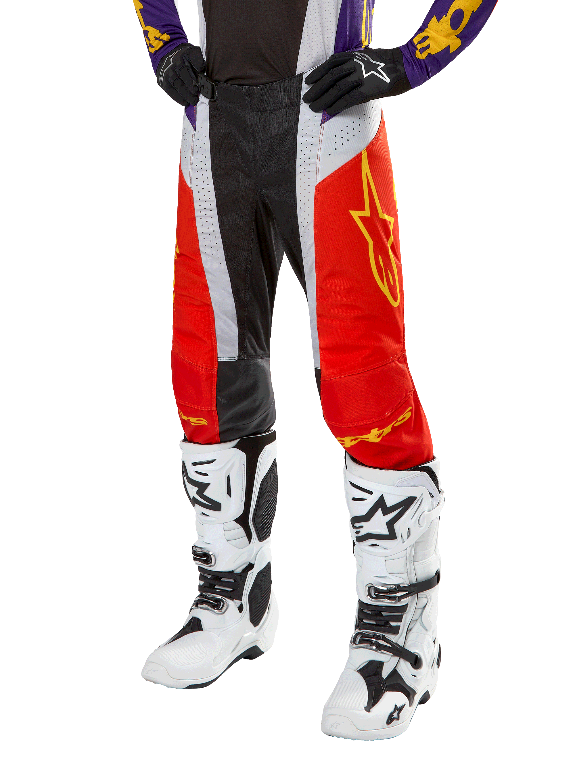 Spodnie Alpinestars Techstar Ocuri 2024, spodnie motocrossowe, jaskrawopomarańczowe, czarne i białe z żółtą grafiką gwiazdy, noszone z fioletową bluzą i białymi butami, wytrzymała odzież wyczynowa do zawodów terenowych