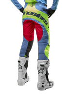 Alpinestars Techstar Ocuri Pants 2024, spodnie motocrossowe, jasnoniebieskie, neonowe żółte i czerwone, widok z tyłu w biało-czarnych butach motocrossowych, wyrazisty design color-blocking i duże logo Alpinestars na siedzeniu