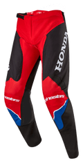 Spodnie Alpinestars Honda Racer Iconic, spodnie motocrossowe, jaskrawoczerwone, czarne i białe z niebieskimi akcentami, z dużym białym logo HONDA na udzie, brandingiem Alpinestars na kolanach, ergonomiczną, wstępnie zakrzywioną konstrukcją nogawek i regulowanym zapięciem zapadkowym w pasie.