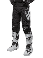 Alpinestars Racer Hana Pants 2024, spodnie motocrossowe, czarne z białymi akcentami i dużym logo, ergonomiczny sportowy design, widoczne białe buty motocrossowe, trwała konstrukcja do jazdy w terenie