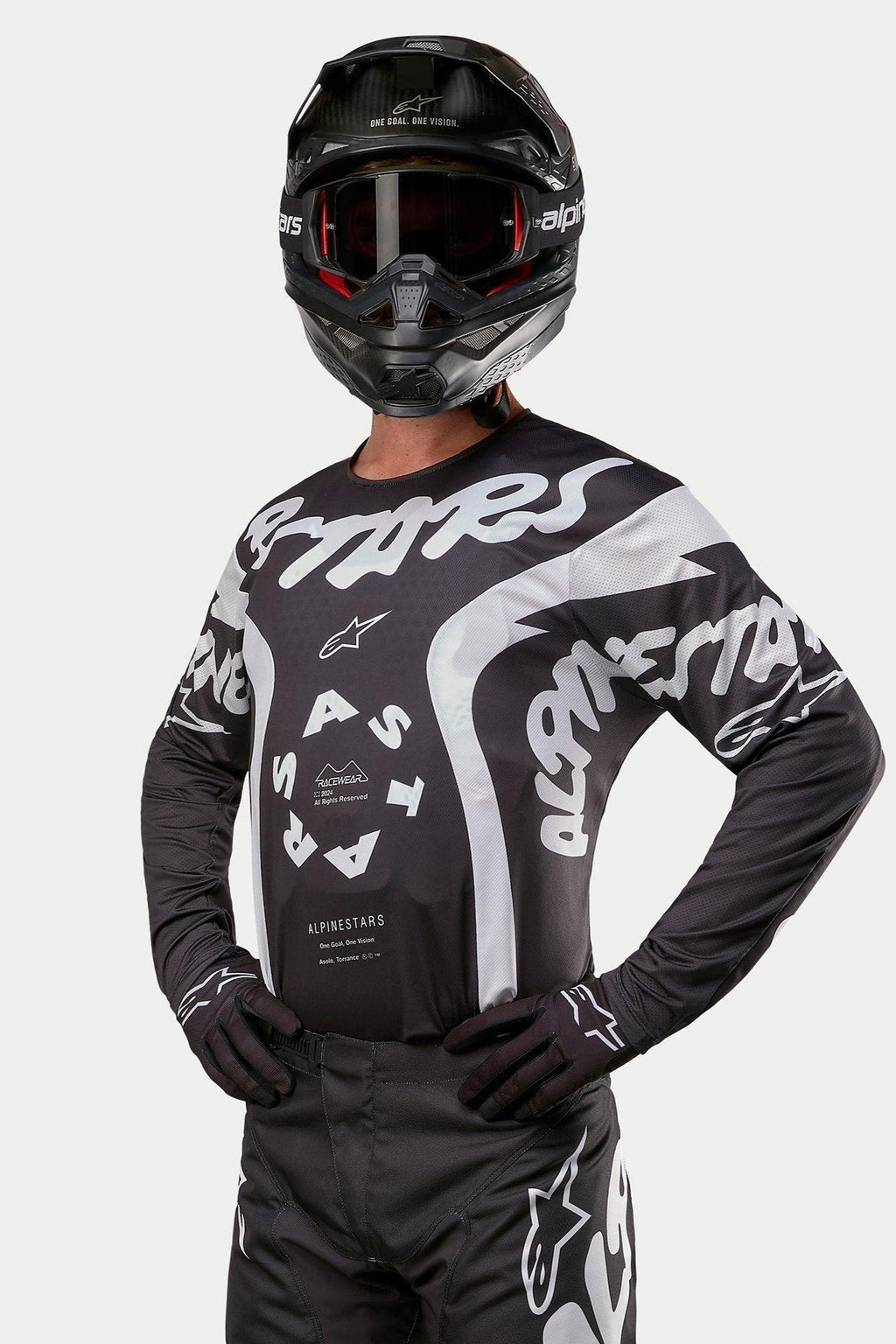 Alpinestars 2024 Racer Hana Jersey, koszulka motocrossowa, czarno-biała, z wyraźną białą grafiką tekstową i logo Alpinestars, noszona przez zawodnika w czarnym kasku i goglach, profesjonalna odzież do wyścigów terenowych