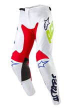 Alpinestars 2024 Racer Hana Pants, spodnie motocrossowe, białe wielokolorowe z czerwonymi i czarnymi panelami na kolanach, niebieskie logo Astars i neonowożółte detale, ergonomiczny krój z zapięciem zapadkowym, wytrzymały materiał do jazdy terenowej