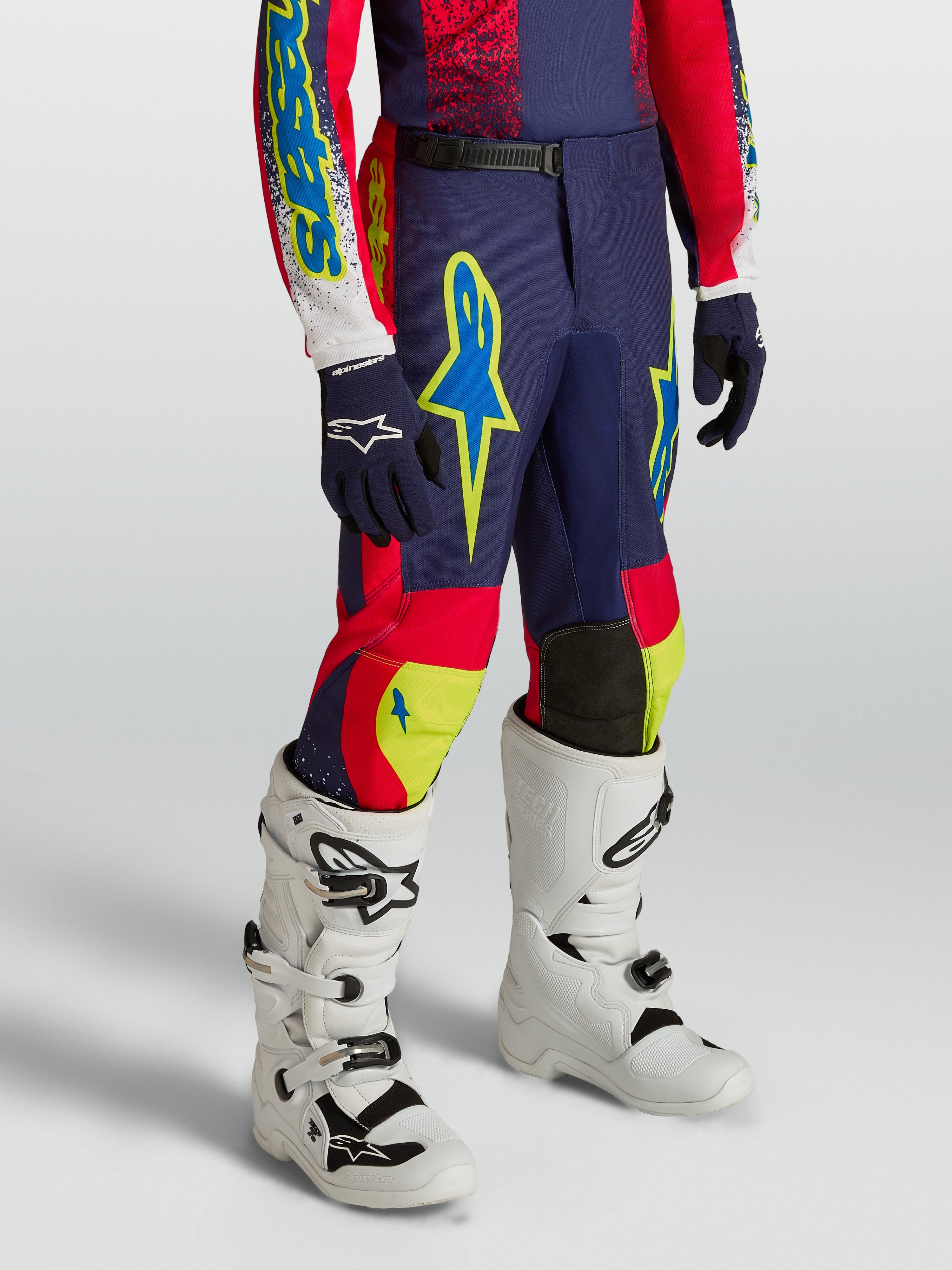 Alpinestars Youth Fluid Drag Pants, navy blue and red motocross racing gear with neon accents and white performance boots.