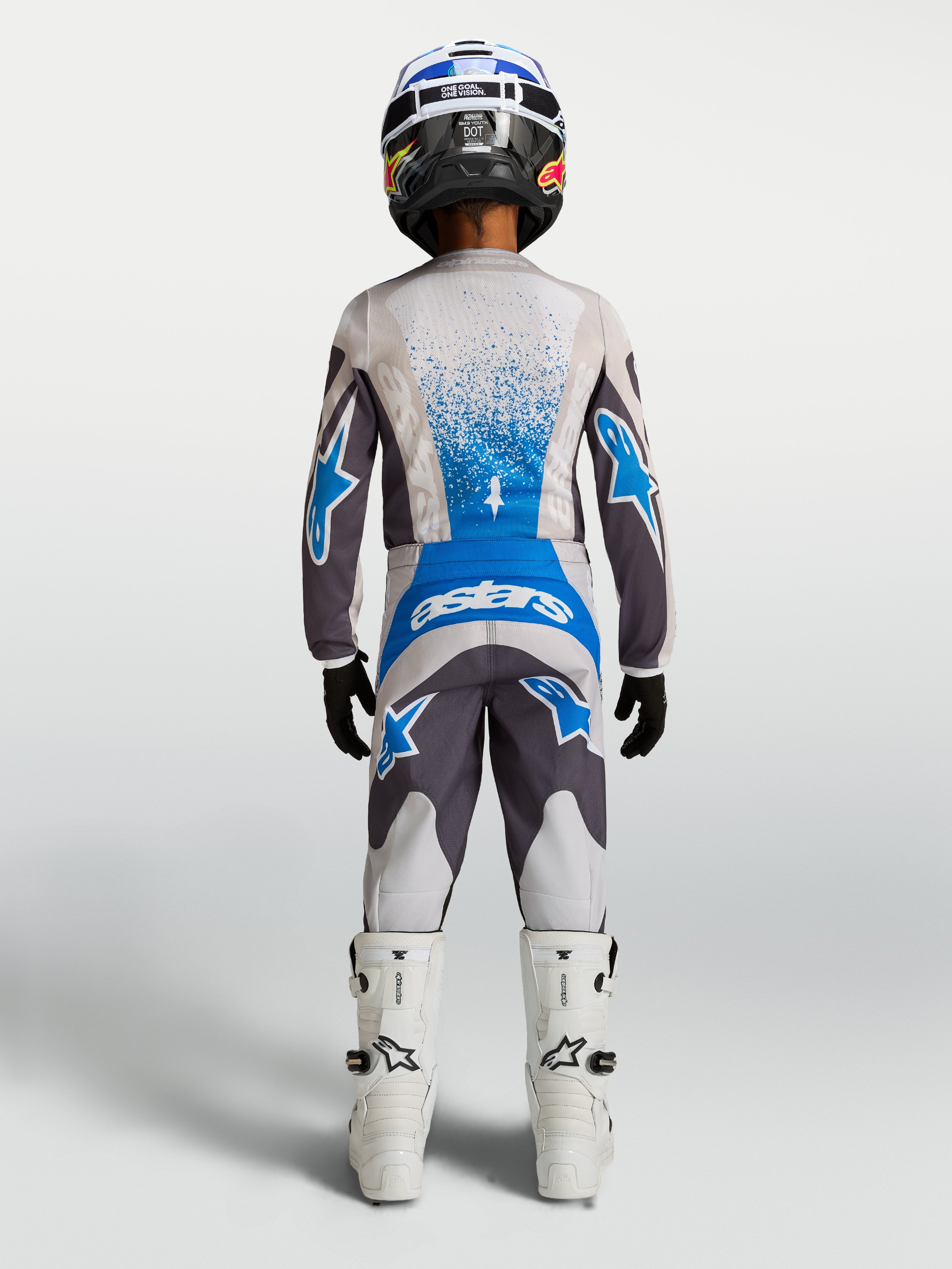 Alpinestars Fluid Drag, młodzieżowe spodnie motocrossowe, szare i niebieskie, widok od tyłu w kompletnym zestawie z koszulką i butami, wytrzymały sprzęt off-road
