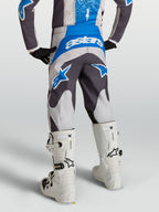 Alpinestars Spodnie Fluid Drag Młodzieżowe, szare i niebieskie spodnie motocrossowe, widok od tyłu na ridera w białych butach.
