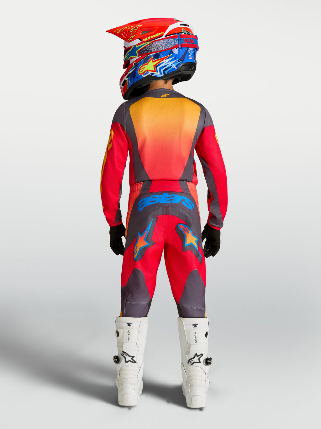 Alpinestars Spodnie Fluid Hunt Młodzieżowe, czerwone i szare spodnie motocrossowe, widok z tyłu, pełny strój i białe buty.