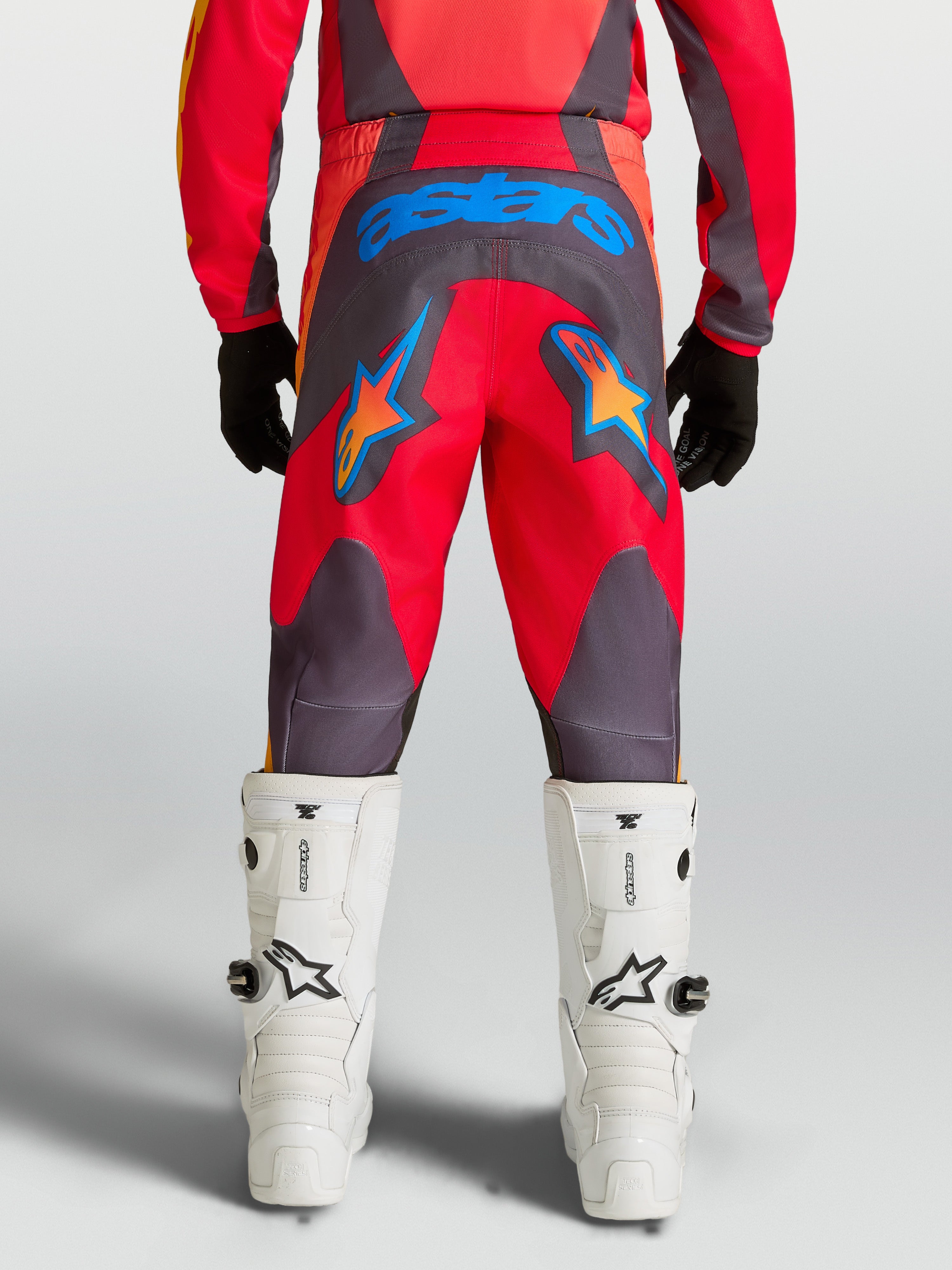 Alpinestars Spodnie Fluid Hunt młodzieżowe, czerwone i szare spodnie MX, widok z tyłu, niebieskie grafiki gwiazd.