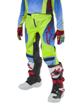 Alpinestars Youth 2024 Racer Hoen Pants, spodnie motocrossowe, żółte neonowe i granatowe z czerwonymi akcentami, zestawione z pasującymi rękawicami oraz białymi, czarnymi i czerwonymi butami, o sportowym kroju z profilowanymi nogawkami do wyścigów off-road