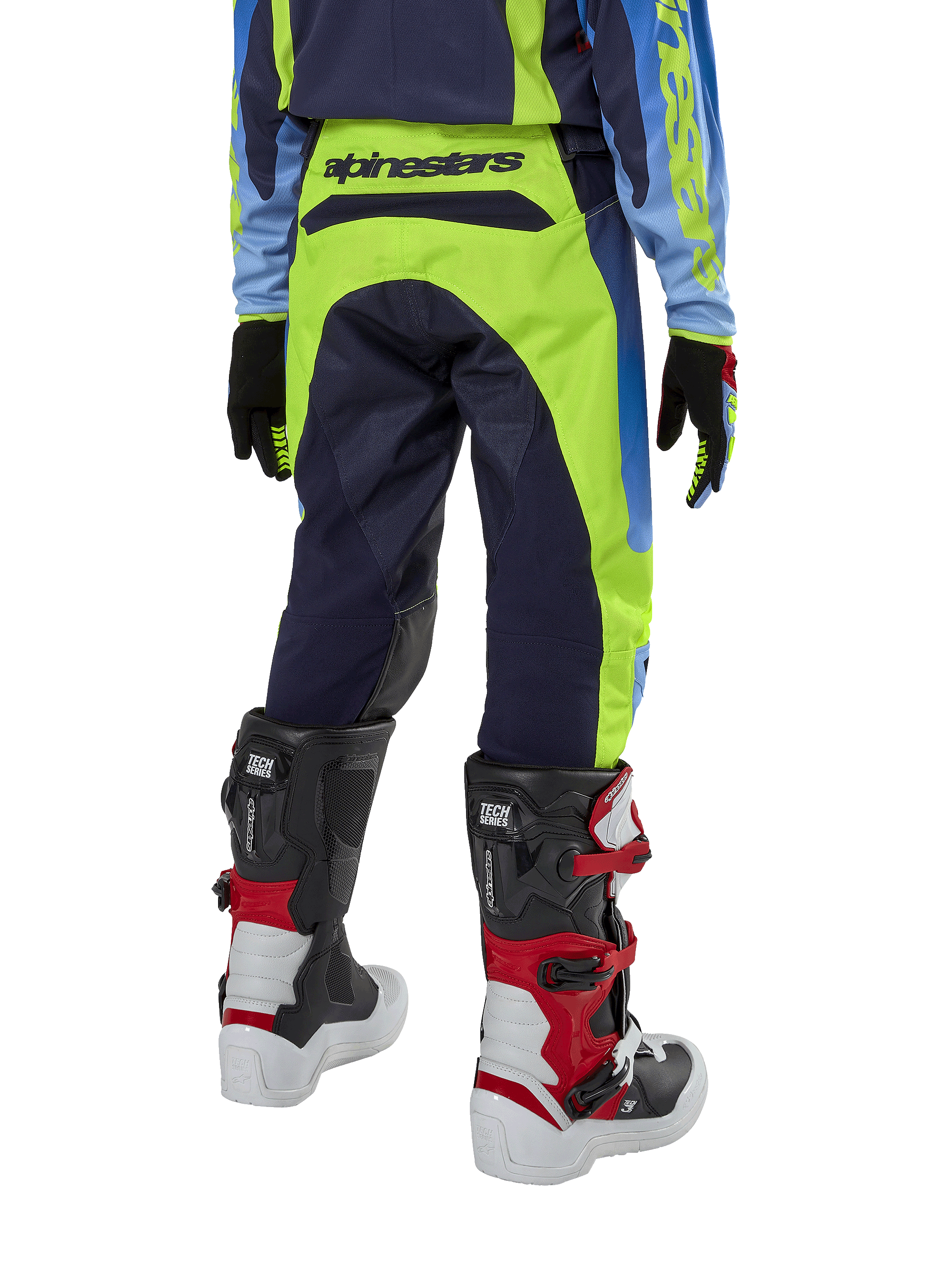 Alpinestars Youth 2024 Racer Hoen Pants, spodnie motocrossowe, żółte fluo i granatowe, widok z tyłu prezentujący wyraźne logo Alpinestars na pasie, noszone z czarno-czerwonymi butami Tech Series i pasującą koszulką, wytrzymały sportowy krój do jazdy terenowej dla młodzieży