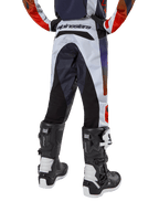 Alpinestars Youth 2024 Racer Hoen Pants, spodnie motocrossowe, jasnoszare z jaskrawopomarańczowymi i czarnymi akcentami, widok z tyłu z czarnymi panelami na siedzeniu i nogawkach, wyraźne logo w pasie z tyłu, noszone z czarno-białymi butami motocrossowymi do jazdy terenowej