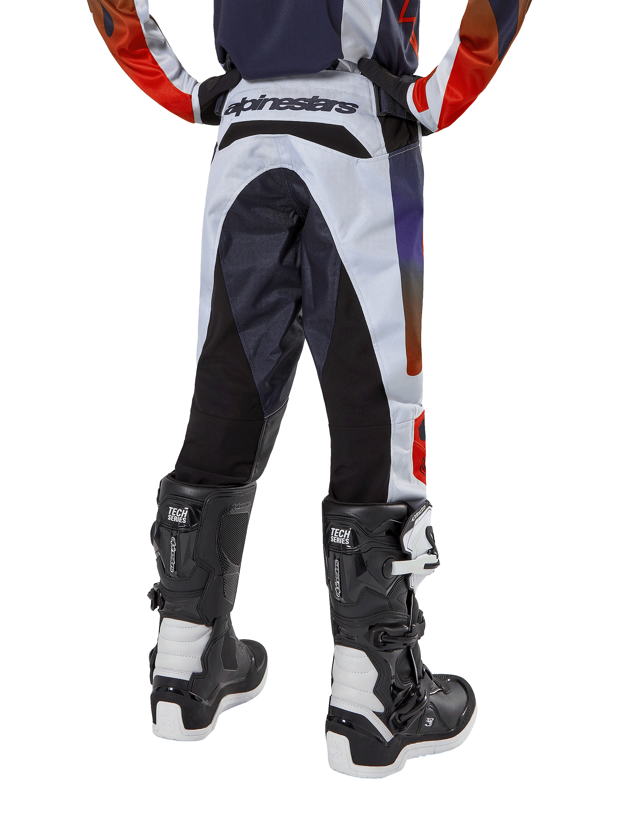 Alpinestars Youth 2024 Racer Hoen Pants, spodnie motocrossowe, jasnoszare z jaskrawopomarańczowymi i czarnymi akcentami, widok z tyłu z czarnymi panelami na siedzeniu i nogawkach, wyraźne logo w pasie z tyłu, noszone z czarno-białymi butami motocrossowymi do jazdy terenowej