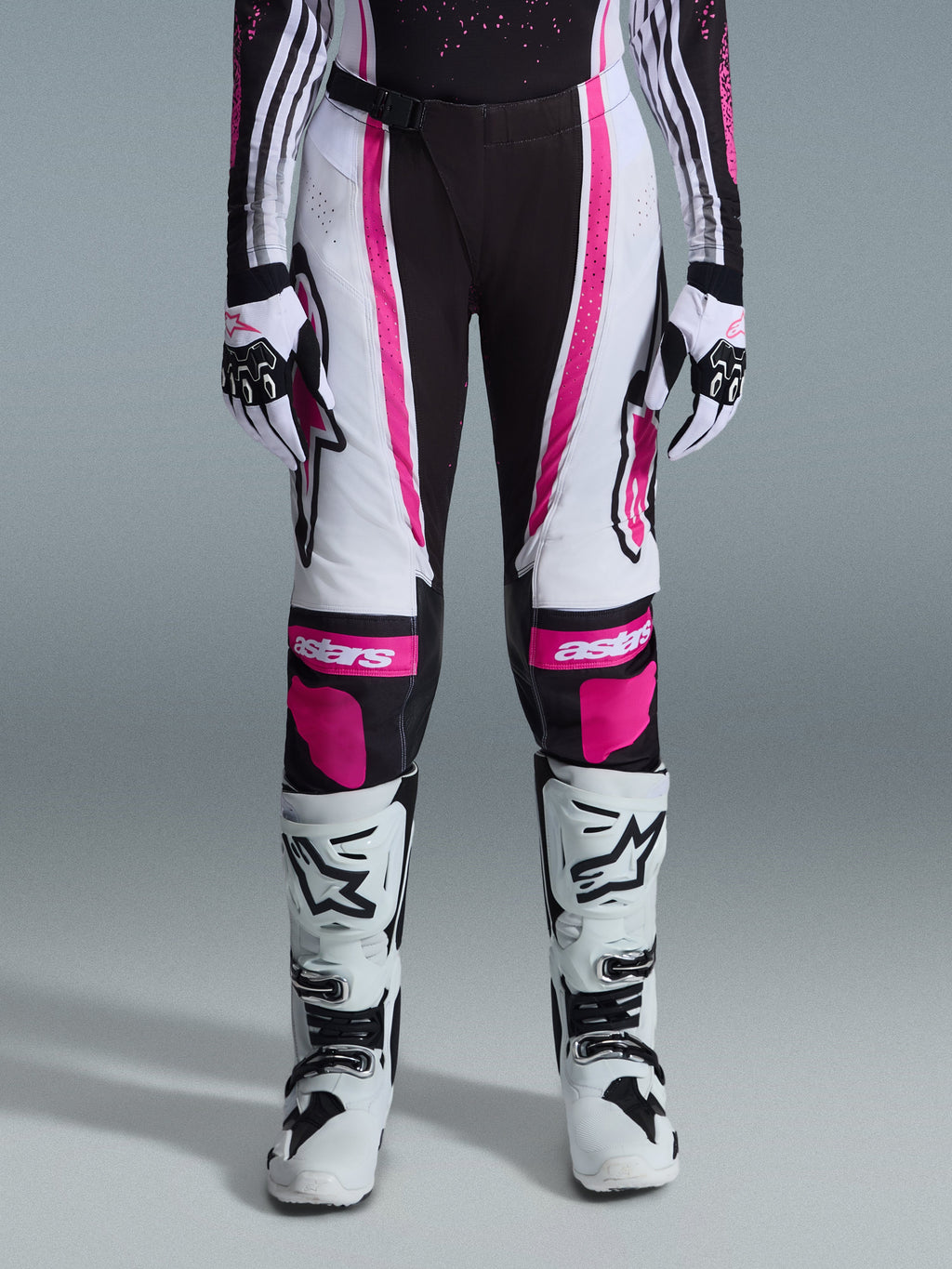 Alpinestars Stella Techstar Nomur 2026, damskie spodnie motocrossowe, czarno-białe z fuksją, noszone z dopasowaną koszulką wyścigową, rękawicami i białymi butami motocrossowymi, z wyrazistymi różowymi grafikami i logo astars na kolanach, zaprojektowane do profesjonalnej rywalizacji off-road.
