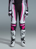 Alpinestars Stella Techstar Nomur 2026, damskie spodnie motocrossowe, czarno-białe z fuksją, noszone z dopasowaną koszulką wyścigową, rękawicami i białymi butami motocrossowymi, z wyrazistymi różowymi grafikami i logo astars na kolanach, zaprojektowane do profesjonalnej rywalizacji off-road.