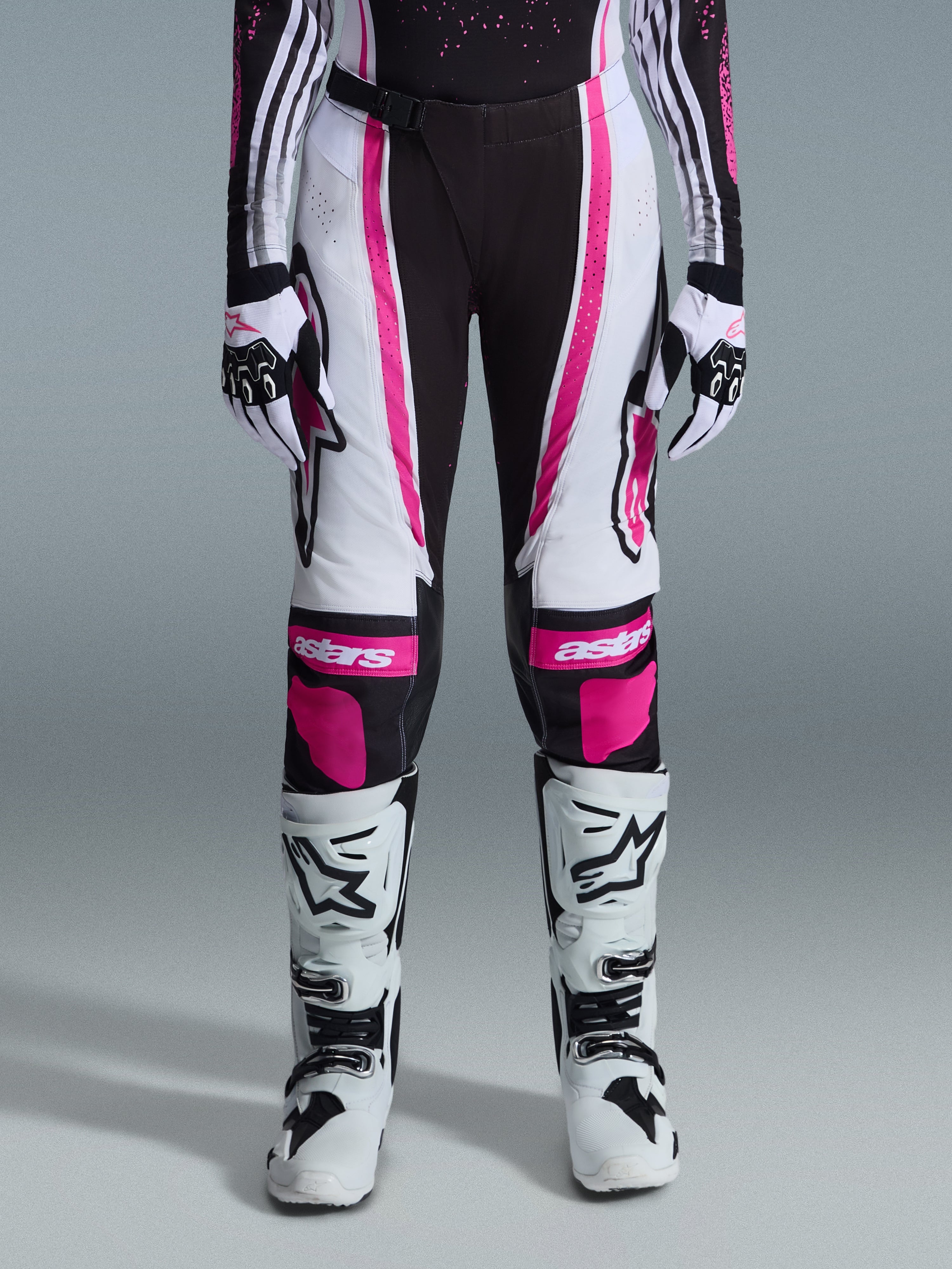 Alpinestars Stella Techstar Nomur 2026, damskie spodnie motocrossowe, czarno-białe z fuksją, noszone z dopasowaną koszulką wyścigową, rękawicami i białymi butami motocrossowymi, z wyrazistymi różowymi grafikami i logo astars na kolanach, zaprojektowane do profesjonalnej rywalizacji off-road.