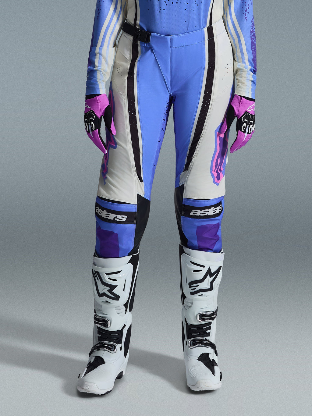 Alpinestars Stella Techstar Nomur 2026, damskie spodnie motocrossowe, jasnoniebieskie, w kolorze złamanej bieli i czarne, zestawione z białymi butami motocrossowymi i różowo-czarnymi rękawicami, z brandingiem „astars” na kolanach i techniczną wielopanelową konstrukcją dla kobiet