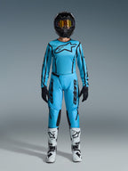 Zestaw Alpinestars 2026 Stella Fluid Apex, damska koszulka i spodnie motocrossowe, niebieski i czarny, z dużym logo gwiazdy na klatce piersiowej, noszony z czarnym kaskiem, przyciemnianymi goglami i białymi butami z czarnymi akcentami, kompletny strój wyścigowy off-road