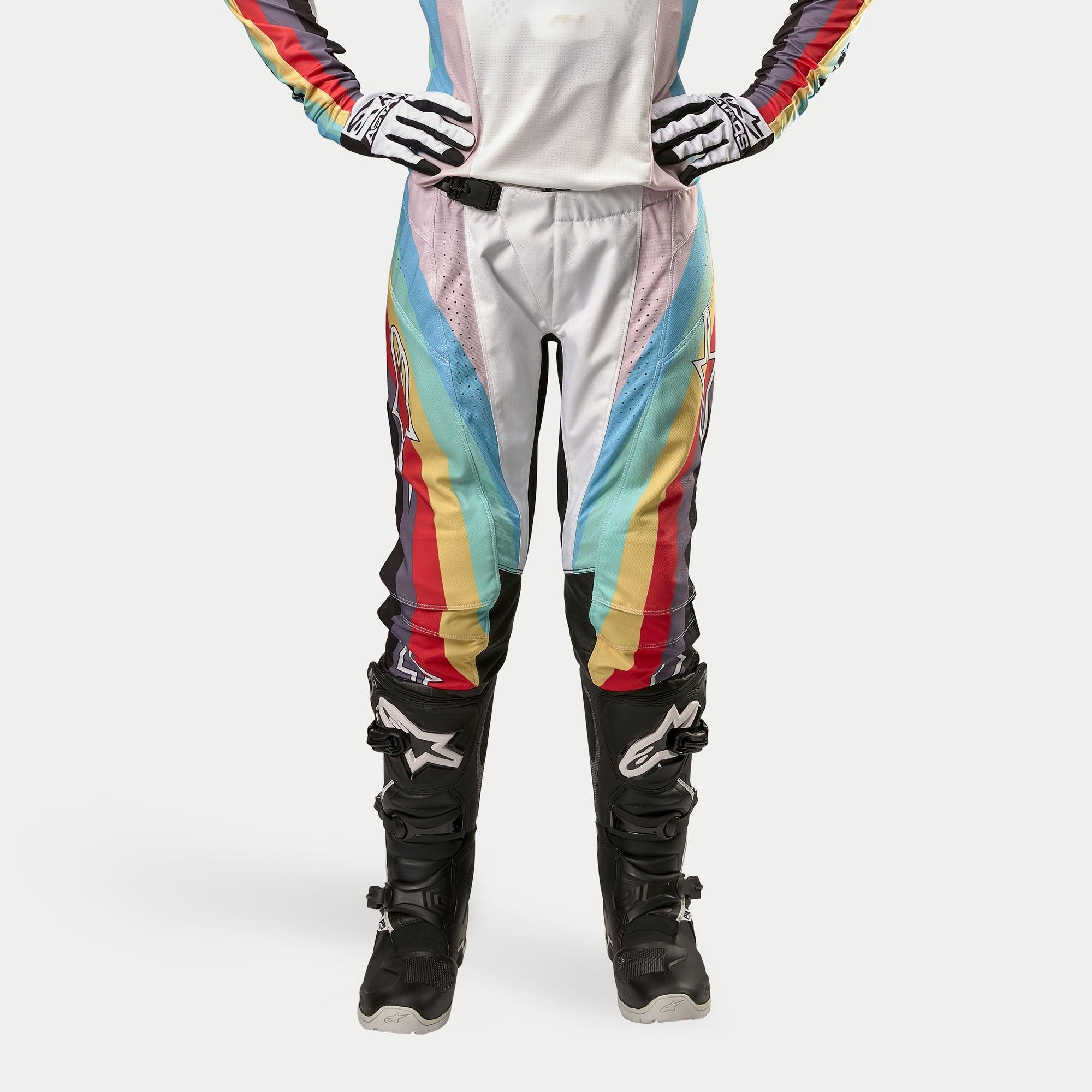 Damskie spodnie Alpinestars Stella Techstar 2024, spodnie motocrossowe, czarne wielokolorowe, z wyrazistymi ukośnymi pasami w kolorach białym, niebieskim, czerwonym i żółtym, prezentowane z czarnymi butami i rękawicami motocrossowymi, sportowy design do jazdy off-road.