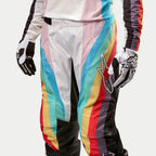 Alpinestars Stella 2024 Techstar Pants, damskie spodnie motocrossowe, czarne wielokolorowe z wyrazistymi ukośnymi pasami w kolorach niebieskim, różowym, żółtym i czerwonym, duże logo gwiazdy na udzie, prezentowane w zestawie z dopasowaną bluzą i rękawicami, profesjonalna odzież do wyścigów terenowych