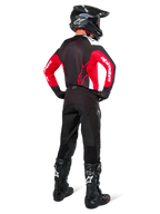 Motocross rider from behind wearing the Alpinestars Pro-Dura Jersey in Black, Bright Red, and White, paired with black motocross pants, helmet, and boots, showing the rear design and sleeve logos, coordinated off-road racing gear.