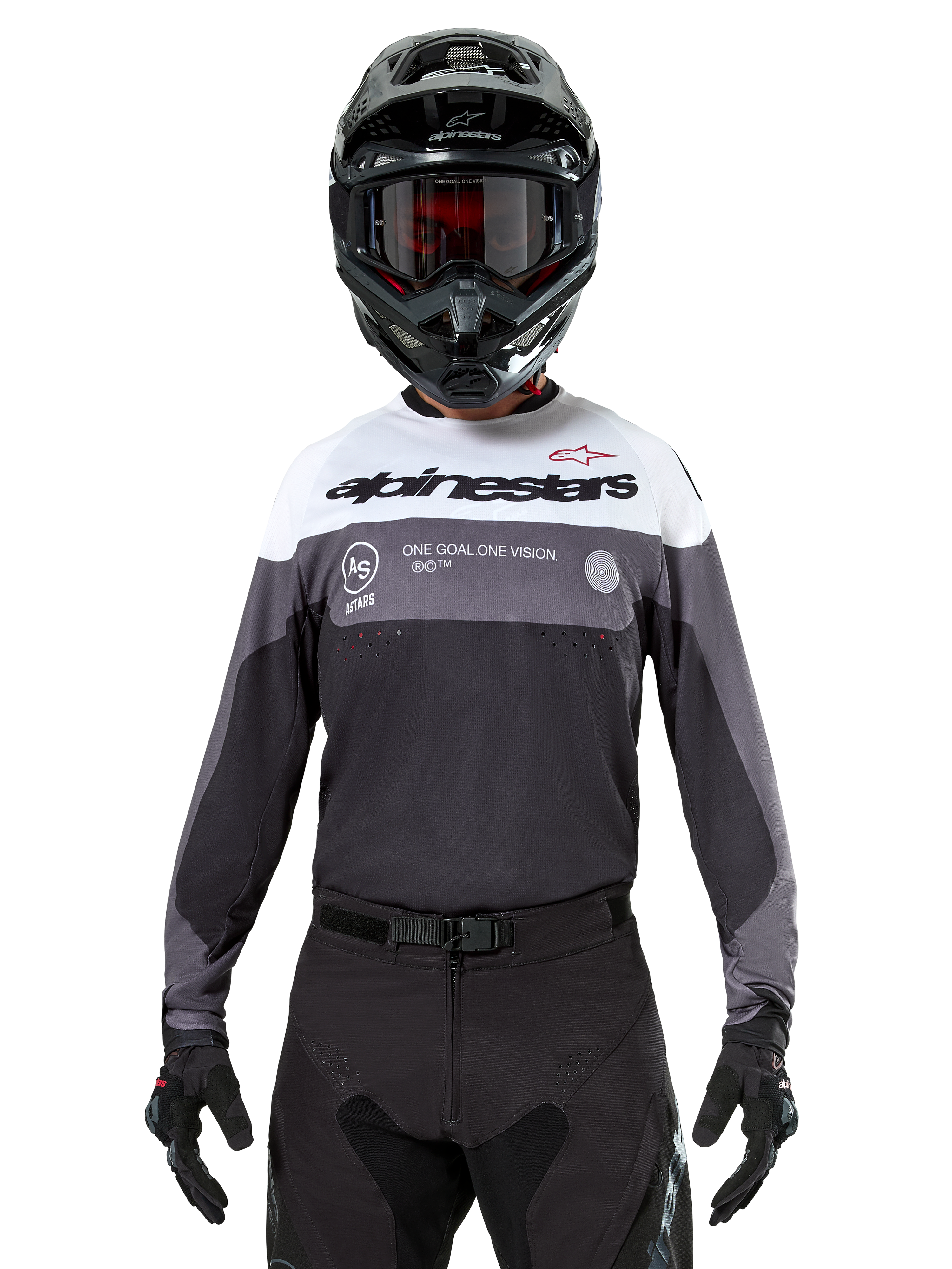 Motocyklista motocrossowy w koszulce Alpinestars Pro-Dura Jersey w kolorze Black Magnet White, sportowa koszulka z długim rękawem z białymi i szarymi blokami kolorystycznymi, czarny kask i gogle, logo „alpinestars” oraz hasło „ONE GOAL ONE VISION”, odzież do wyścigów motocyklowych off-road