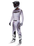 Alpinestars 2025 Supertech Maker Gear Set, kompletny strój motocrossowy, biało-szary gradient z czarnymi logotypami i czerwonymi akcentami, zawiera kask z goglami, koszulkę, spodnie, białe buty i rękawice, nowoczesny, wyczynowy design do wyścigów terenowych