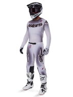 Motocrossowiec w koszulce Alpinestars 2025 Supertech Maker w kolorze srebrnym i czarnym, pasujące srebrno-czarne spodnie, czarno-biały kask z czarnymi goglami, biało-czarne buty i dopasowane rękawice, profesjonalny design z gradientem do wyścigów terenowych