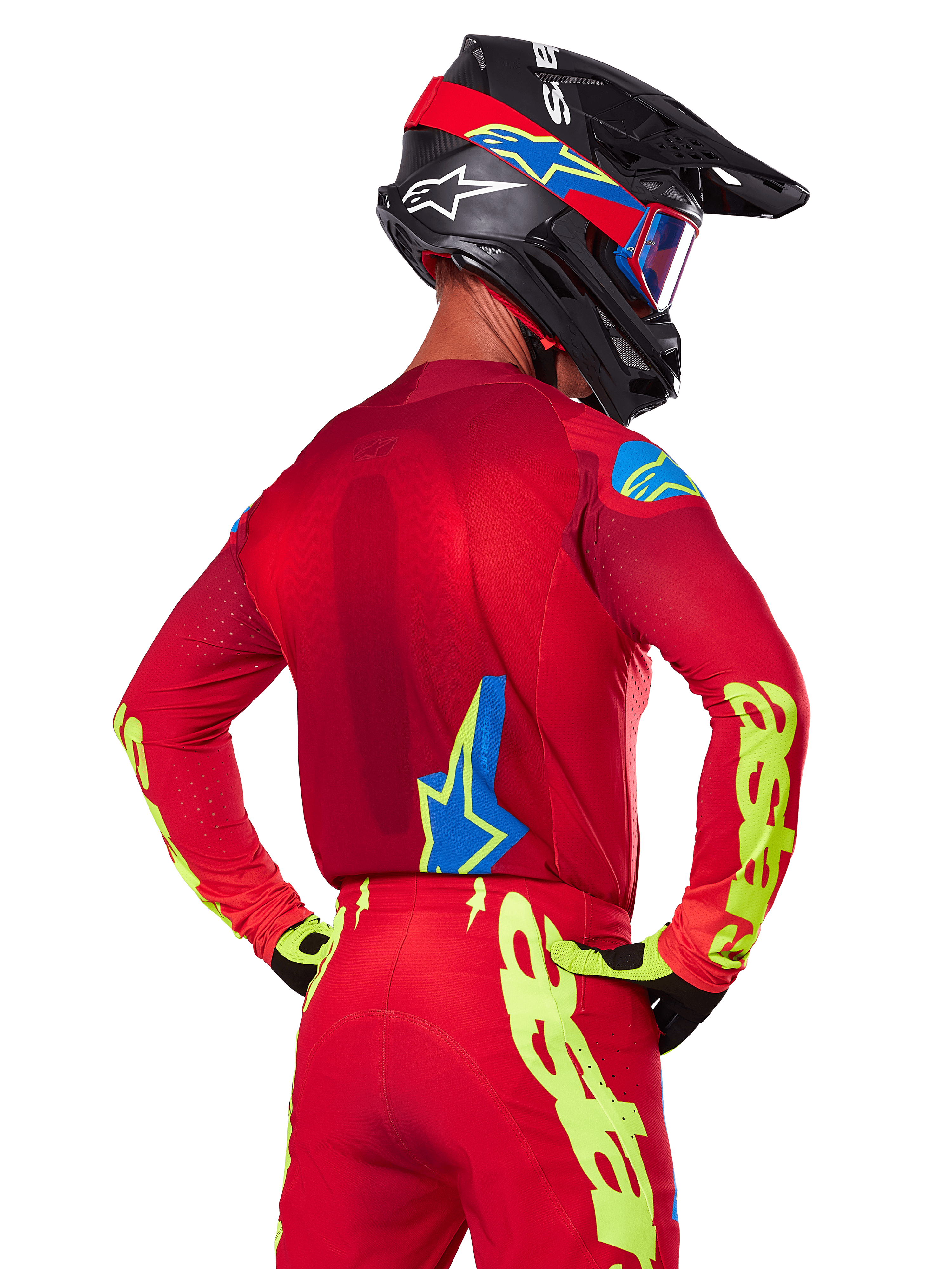 Rear view of a motocross rider wearing the Alpinestars 2025 Supertech Maker Gear Set in Red, featuring a red jersey with neon yellow branding on the sleeves, matching red pants, a black helmet with blue and red accents, and coordinating black and yellow gloves.