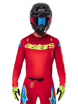 Alpinestars 2025 Supertech Maker Jersey in Bright Red Yellow Fluo, featuring yellow 'astars' chest branding and blue star shoulder designs, worn with matching pants, black helmet, blue goggles, and yellow gloves, professional motocross racing apparel