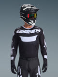 Alpinestars 2026 Racer Air Riway Jersey, czarno-biała koszulka motocrossowa z brandingiem „astars”, noszona przez motocyklistę w pasującym czarnym kasku, goglach i spodniach, z oddychającymi panelami z siatki do wyścigów terenowych.