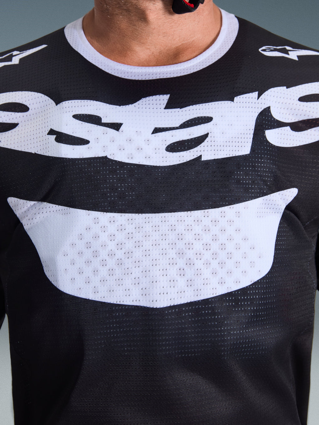 Alpinestars 2026 Racer Air Riway Jersey, koszulka motocrossowa, czarno-biała, zbliżenie na klatkę piersiową pokazujące dużą białą grafikę i oddychającą konstrukcję z siateczki, biały kołnierzyk i logo na ramionach