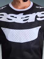 Alpinestars 2026 Racer Air Riway Jersey, koszulka motocrossowa, czarno-biała, zbliżenie na klatkę piersiową z dużym białym logo, szczegółowa tekstura siatkowego materiału zapewniającego przepływ powietrza, techniczna oddychająca odzież do jazdy off-road