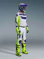 Motocyklista motocrossowy ubrany w zestaw Alpinestars 2026 Racer Air Riway w kolorach jasnoszarym, żółtym fluo i niebieskim. Zestaw zawiera siateczkową koszulkę z długim rękawem, pasujące spodnie wyścigowe, jaskrawe neonowo-żółte rękawice i buty oraz fioletowo-niebieski kask z goglami, zaprojektowany z myślą o wentylowanej wydajności w terenie.
