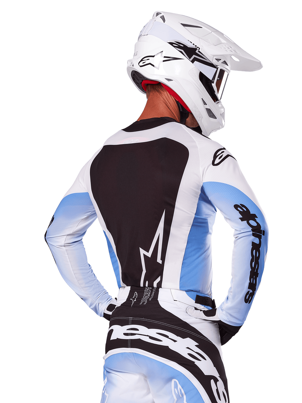 Widok od tyłu zawodnika motocrossowego w zestawie Alpinestars 2025 Techstar Melt w kolorze biało-niebieskim, koszulka z dużym czarnym panelem na plecach i białym logo gwiazdy, jasnoniebieskie rękawy z gradientem, dopasowane biało-niebieskie spodnie, biały kask wyścigowy i czarno-białe rękawice, profesjonalny strój do motocrossu