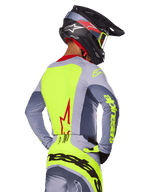 Alpinestars 2025 Techstar Melt Jersey, Bright Red Gray, widok z tyłu zawodnika motocrossowego w szaro-neonowo-żółtym stroju wyścigowym, czerwone logo gwiazdy na plecach, pasujący czarno-czerwony kask, wyczynowa odzież off-road