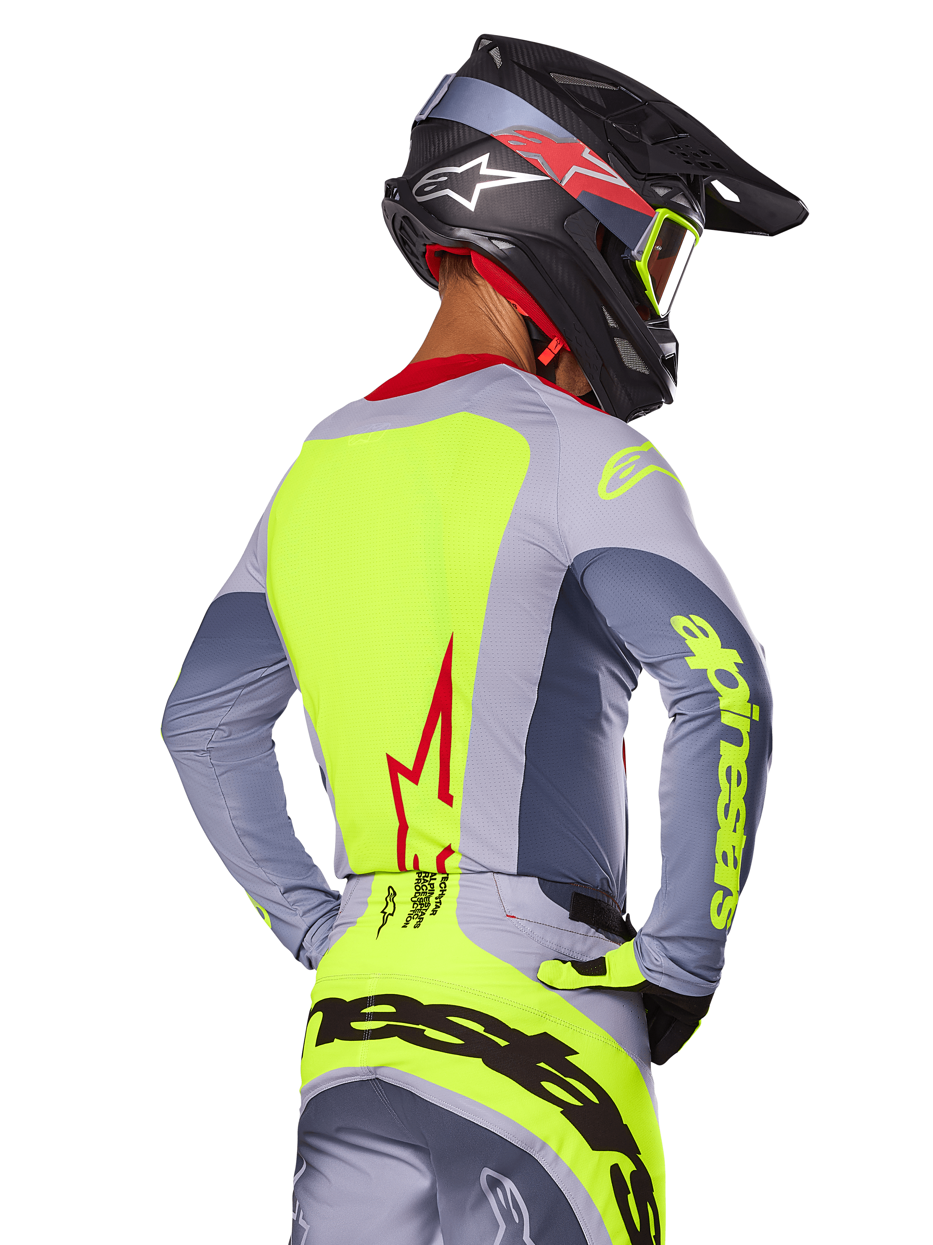 Alpinestars 2025 Techstar Melt Jersey, Bright Red Gray, widok z tyłu zawodnika motocrossowego w szaro-neonowo-żółtym stroju wyścigowym, czerwone logo gwiazdy na plecach, pasujący czarno-czerwony kask, wyczynowa odzież off-road