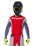 Motocrossista ubrany w koszulkę Techstar Melt 2025 i pasujące spodnie, jasnoczerwone i szare z białym brandingiem Alpinestars, czarny kask z neonowożółtymi goglami, pasujące neonowożółte rękawice, wentylowana odzież wyczynowa do wyścigów terenowych